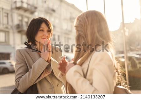 Cute fair-skinned adult brunette lady is touched looking at blonde while standing outdoors. Old acquaintances are happy to meet each other on warm day. People and free time concept Royalty-Free Stock Photo #2140133207