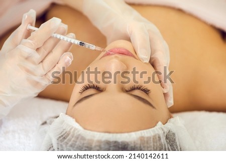 Woman getting professional beauty treatment. Young lady receiving injection for beautiful, bigger, plumper, fuller lips. Hands holding syringe above face in close up. Aesthetic medicine concept
