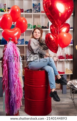 aerodesigner. a attractive woman on a red decorative barrel with a large red balloons in the shape of a heart. valentine's day. sale of compositions from balls.