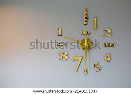 Wall clock with gold numbers on a white background with space to insert text.