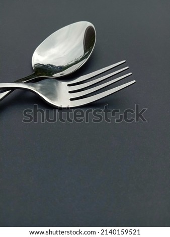 Part of a stainless steel spoon and fork isolated on a dark gray background. Selective focus.