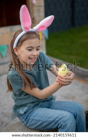 a cute girl in bunny ears is holding a chicken. Happy easter.