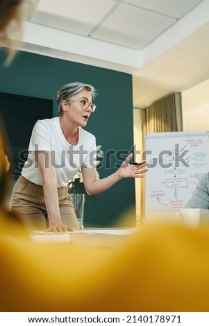 Experienced business professional leading a discussion with her team in a boardroom. Businesspeople sharing creative ideas during a meeting in a modern workplace. Royalty-Free Stock Photo #2140178971