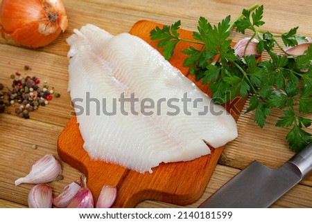 Fresh raw halibut fillet with greens and spices on wooden background. Cooking ingredients
