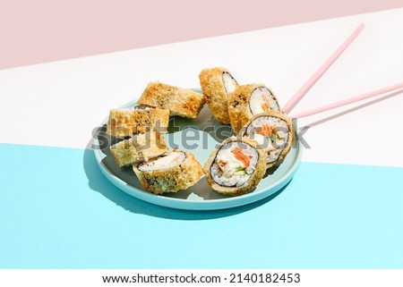 Tempura maki roll with salmon and eel on ceramic plate. Hot sushi with eel, salmon, cheese and cucumber inside. Modern japanese menu concept. Maki sushi on coloured background with chopsticks
