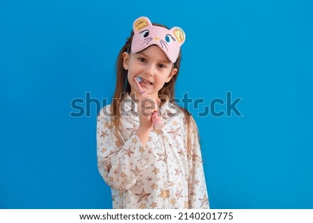 Cute little baby girl is brushing her teeth in pajamas on a blue background. Space for text. Healthy teeth.