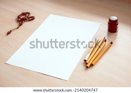 Blank sheet of paper with traditional Arabic kalams and ink for calligraphy and prayer beads on the table