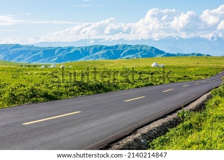 Empty asphalt road and green grassland and mountain under blue sky in Xinjiang, China. 