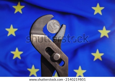 Coin one ruble is clamped in a wrench against the background of the flag of European Union. The idea of the collapse of the ruble and economy sanctions against Russia.