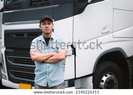 Asian Truck Driver Standing Cross One's Arm with Semi Trailer Trucks. Mechanic Repairman Auto Service Shop. Cargo Shipping Freight Truck Transport Logistics. Royalty-Free Stock Photo #2140226311
