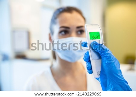 A pandemic workplace environment. Office workers wear face coverings to protect the spread of virus doing the Covid-19  Coronavirus outbreak. Body temperature is checked with a infrared thermometer.