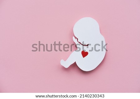 Paper silhouette of a human embryo with a red heart on a pink background. Flat lay, place for text. Royalty-Free Stock Photo #2140230343