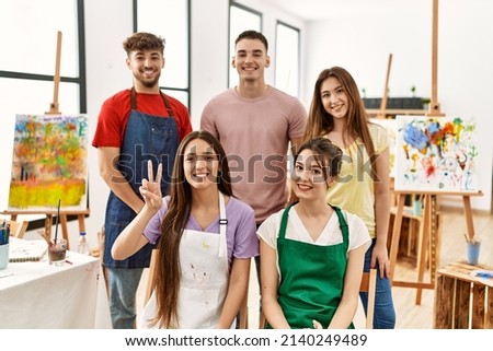 Group of five hispanic artists at art studio showing and pointing up with fingers number two while smiling confident and happy. 