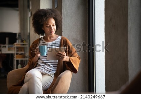 Enjoying coffee break with tablet. Attractive black business woman working on digital tablet