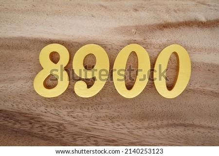 Wooden  numerals 8900 painted in gold on a dark brown and white patterned plank background.