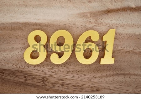 Wooden  numerals 8961 painted in gold on a dark brown and white patterned plank background.