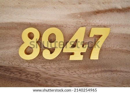 Wooden  numerals 8947 painted in gold on a dark brown and white patterned plank background.