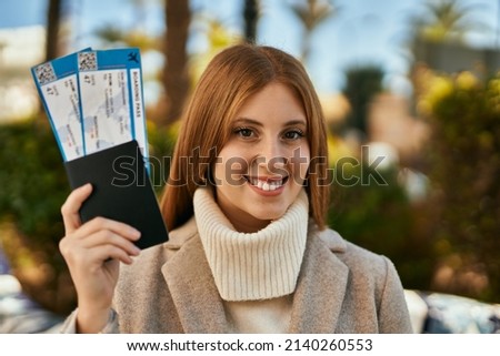 Young redhead girl smiling happy holding passport and boarding pass at the city.