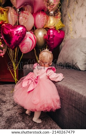 Little girl in a pink dress near the balloons. Baby girl's first birthday 