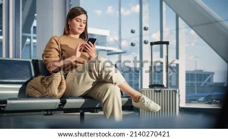 Airport Terminal: Woman Waits for Flight, Uses Smartphone, Browse Internet, Social Media, Online Shopping. Traveling Female Remote Work Online on Mobile Phone in a Boarding Lounge of Airline Hub Royalty-Free Stock Photo #2140270421