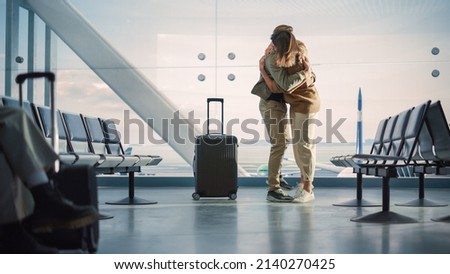Airport Terminal Family Reunion: Beauitful Couple Meets at the Boarding Lounge. Smiling Girlfiend Meets the Love of Her Life after Long Parting and Hugs and Dances with Her Handsome Partner Royalty-Free Stock Photo #2140270425