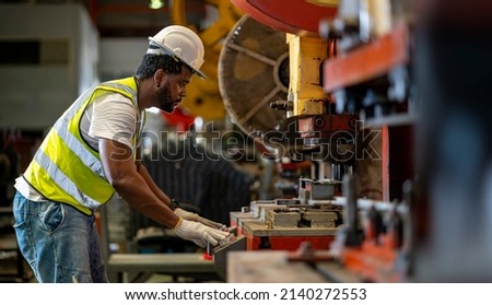 African American industrial worker is using hydraulic power press machine to make metal and steel part while working inside the metal sheet galvanized roof factory for safety industry Royalty-Free Stock Photo #2140272553