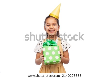 birthday, childhood and people concept - portrait of smiling little girl in dress and party hat with gift box over white background
