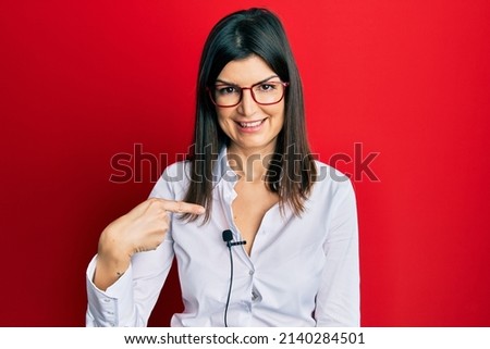 Young hispanic woman using lavalier microphone smiling happy pointing with hand and finger 