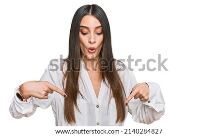 Young beautiful woman wearing casual white shirt pointing down with fingers showing advertisement, surprised face and open mouth 