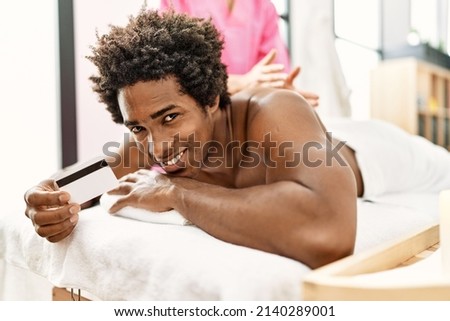 Young african american man having massage holding credit card at beauty center