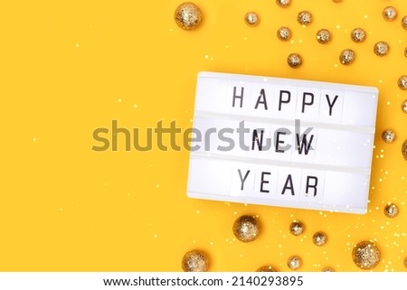 Happy New Year. Lightbox and golden round glittering confetti on a yellow background with copy space.