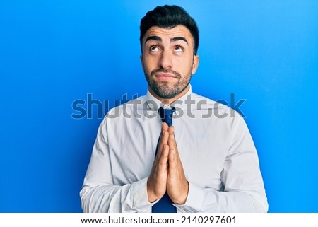 Young hispanic man wearing business clothes begging and praying with hands together with hope expression on face very emotional and worried. begging. 