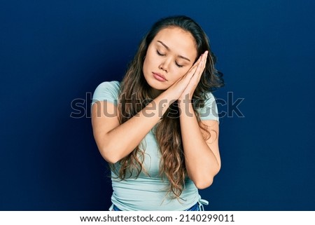 Young hispanic girl wearing casual clothes sleeping tired dreaming and posing with hands together while smiling with closed eyes. 