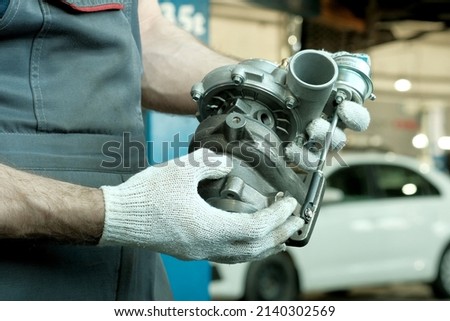 Repair and maintenance in the car center. An auto mechanic holds a turbine in his hands. Inspection and control of spare parts. Checking the conformity and integrity of the turbine before installing i Royalty-Free Stock Photo #2140302569