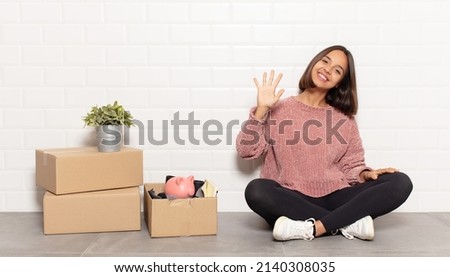 hispanic woman smiling and looking friendly, showing number five or fifth with hand forward, counting down