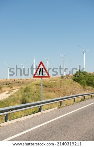 Traffic sign warning of narrow road ahead, in area near wind farm