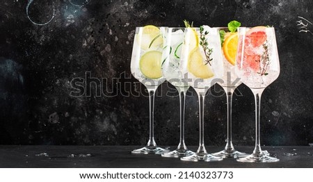 Gin and tonic cocktails set. Trendy Alcoholic drinks with lime, lemon, grapefruit, orange, cucumber, soda and spicy herbs in wine glasses, black background. Summer cocktail party