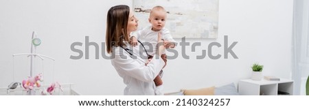 Young family doctor in white cot holding baby boy at home, banner