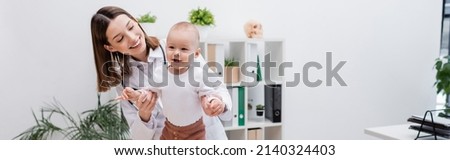 Young family doctor holding hands of baby in hospital, banner Royalty-Free Stock Photo #2140324403