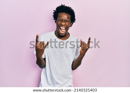 Young african american man wearing casual white t shirt shouting with crazy expression doing rock symbol with hands up. music star. heavy concept. 