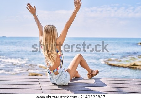 Young blonde girl on back view with hands raised up at the beach.