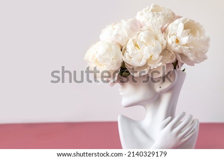 Fresh bunch of white peonies in vase in shape of womens face on dusty pink background. Trendy Ceramic Vase of human head, Handmade Modern Statue Art Flower Vase. Card Concept, copy space for text Royalty-Free Stock Photo #2140329179