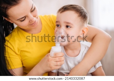 a little girl cries when inhaled with a nebulizer. A child with a viral disease in an inhalation mask is sitting in his mother's arms. Patient with asthma. Royalty-Free Stock Photo #2140332087