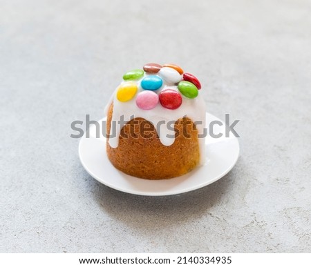 Festive Easter cake with icing sugar, decorated with colorful dragees, on a plate. Light grey background