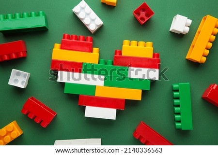 Photo of a heart made from a children's constructor with a pixel art technology lies on the green background. Top view.