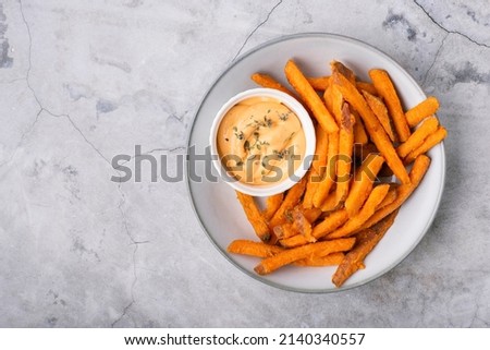Baked sweet potato fries on a plate with savory sauce over concrete background, top view