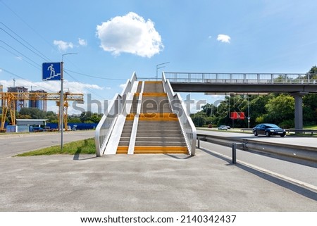 A pedestrian overpass across a busy city highway provides access from a microdistrict under construction to a green city park. ?opy space. Royalty-Free Stock Photo #2140342437