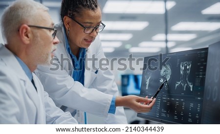 Medical Hospital: Neurologist and Neurosurgeon Talk, Use Computer, Analyse Patient MRI Scan, Diagnose Brain. Health Clinic Lab: Two Professional Physicians Look at Functoning CT Scan Find Treatment Royalty-Free Stock Photo #2140344439