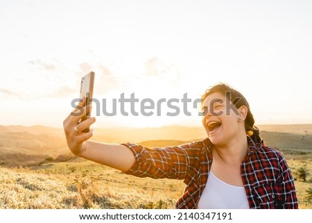 Beautiful Caucasian woman taking a selfie on the mountain very happy with a beautiful sunset.