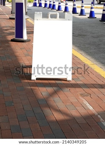 White blank sandwich board sign on a brick sidewalk near a driveway
